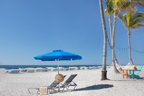 Una platja amb gandules, un para-sol blau i palmeres.