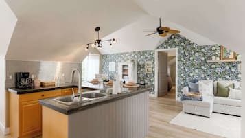 A modern kitchen with a central island, a dining area with a white sofa, and a ceiling fan.