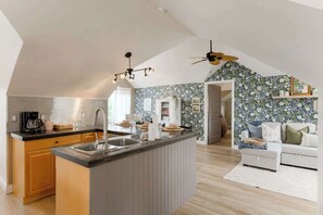 A modern kitchen with a central island, a dining area with a white sofa, and a ceiling fan.