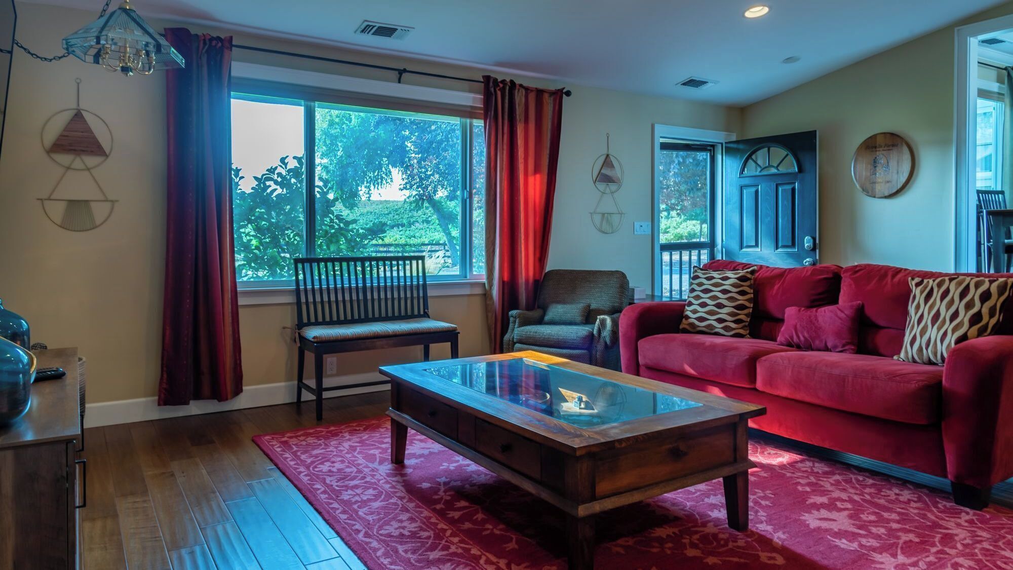 A living room with a red sofa, a wooden coffee table, a chair, and a window with curtains.