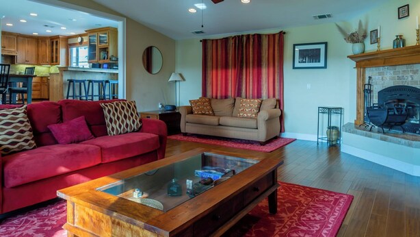 Ein Wohnzimmer mit einem roten Sofa, einem beigen Sofa und einem Glastisch. Ein Kamin mit Steinverkleidung und ein roter Vorhang sind ebenfalls vorhanden.