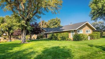 A single-story house with a sloped roof, surrounded by a well-maintained lawn and mature trees.