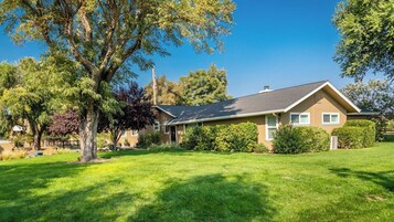 A single-story house with a sloped roof, surrounded by a well-maintained lawn and mature trees.