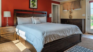 Una camera da letto con un letto grande, due comodini, un tavolino, una lampada a parete, un quadro incorniciato e una finestra con tende.
