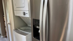 Cocina compacta con lavadora y secadora integradas, refrigerador de acero inoxidable y una ventana pequeña.