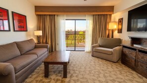 Ein Hotelzimmer mit Sofa, Sessel, Couchtisch und einem Fernseher auf einer Holzkommode.