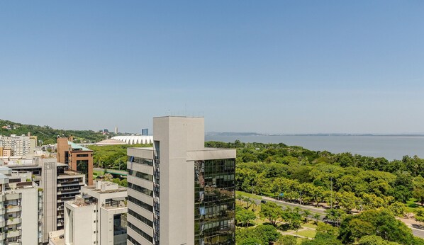 A high-rise building with a modern design, surrounded by lush greenery and a view of a body of water.