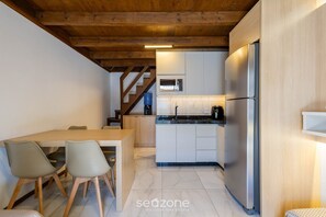 A compact kitchen with a built-in microwave, a stainless steel refrigerator, and a wooden dining table with chairs. - Charming Cottage w/ Balcony Near the Beach Vil0002 (Penha)