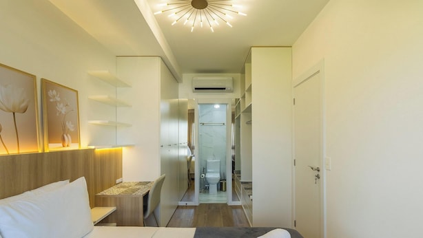 Habitación de hotel con cama, mesitas de noche, una repisa en la pared con obras de arte, una lámpara de techo y un equipo de aire acondicionado.