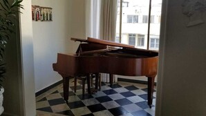 Un piano de cola en una habitación con piso a cuadros, una ventana con cortinas y una pared con cuadros enmarcados.