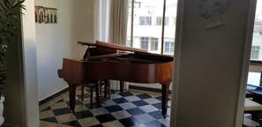 A grand piano in a room with a checkered floor, a window with curtains, and a wall with framed pictures. - Room in a large apartment in Copacabana, with en-suite bathroom. (Rio de Janeiro)