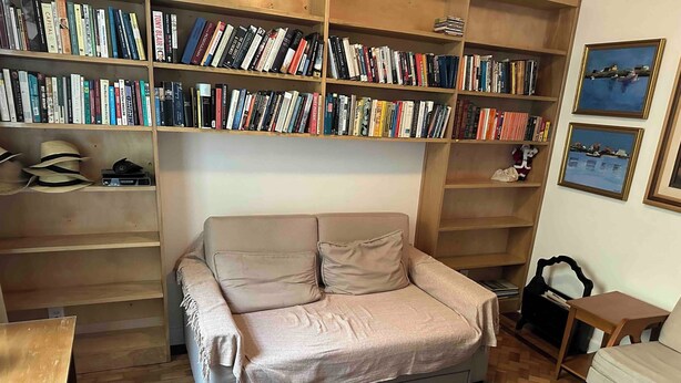 Una sala de estar acogedora con un sofá, una estantería llena de libros, una mesita y una alfombra estampada.