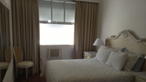 Una habitación de hotel con cama, una silla, una mesita de noche y una ventana con cortinas.