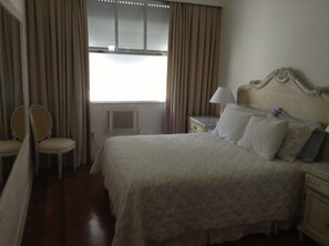 A hotel room with a bed, a chair, a nightstand, and a window with curtains. - Room in a large apartment in Copacabana, with en-suite bathroom. (Rio de Janeiro)