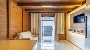 Een modern interieur met een houten plafond, een bank, een eettafel, een aan de muur bevestigde televisie en een schuifdeur naar een buitenruimte.
