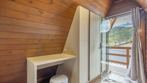 Interior em madeira com box de vidro e vista para uma paisagem montanhosa.