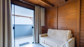 A room with a wooden wall, a white sofa, and a sliding glass door with curtains.