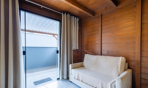 A room with a wooden wall, a white sofa, and a sliding glass door with curtains. - Chalet in Condo w/ Barbecue and Bonfire Vil0004 (Penha)