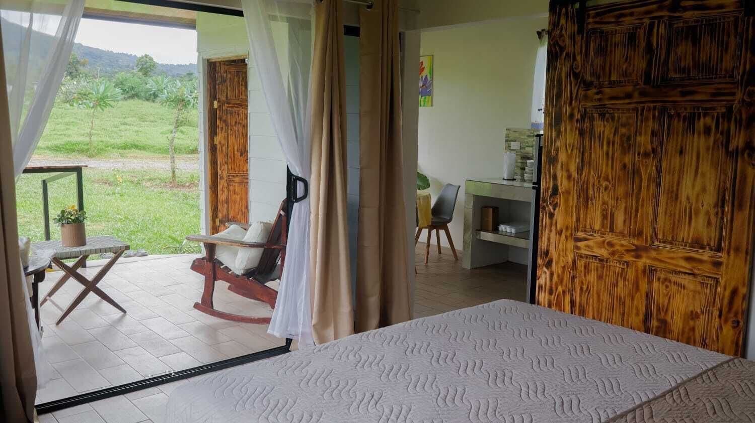 A room with a bed, a chair, a table, and a view of a green landscape.