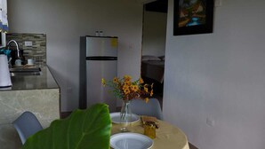 Uma sala de jantar com uma mesa posta para dois, uma geladeira e um vaso com flores.