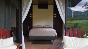 Quarto com cama, cortinas, mesa de cabeceira e vista para o exterior.