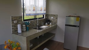 Una cocina con un refrigerador de acero inoxidable, un lavamanos y una ventana con cortina.