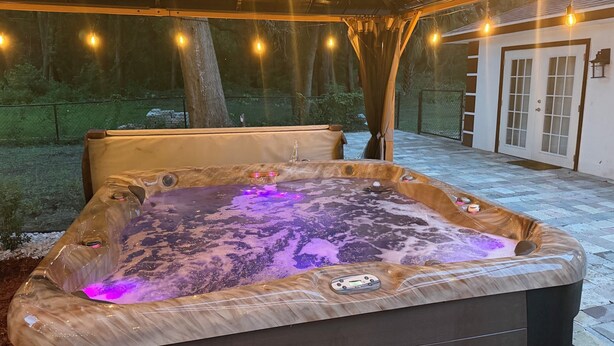 Un jacuzzi con panel de control y exterior de madera, rodeado por un porche cubierto con luces colgantes.