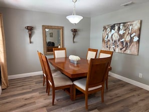 A dining room with a wooden table, six chairs, a vase of flowers, a large mirror, and a painting on the wall. - Fireline's Ocala Retreat Near WEC, Springs Hot Tub! (Ocala City)