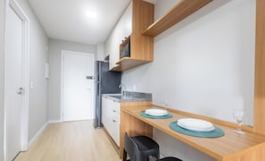 A compact kitchen with a refrigerator, microwave, and wooden shelves. - Complete Studio in Perdizes Cep00428 (São Paulo)