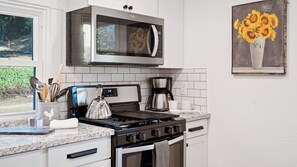 Una cucina moderna con un forno a microonde in acciaio inossidabile, un bollitore, una macchina da caffè e un fornello.