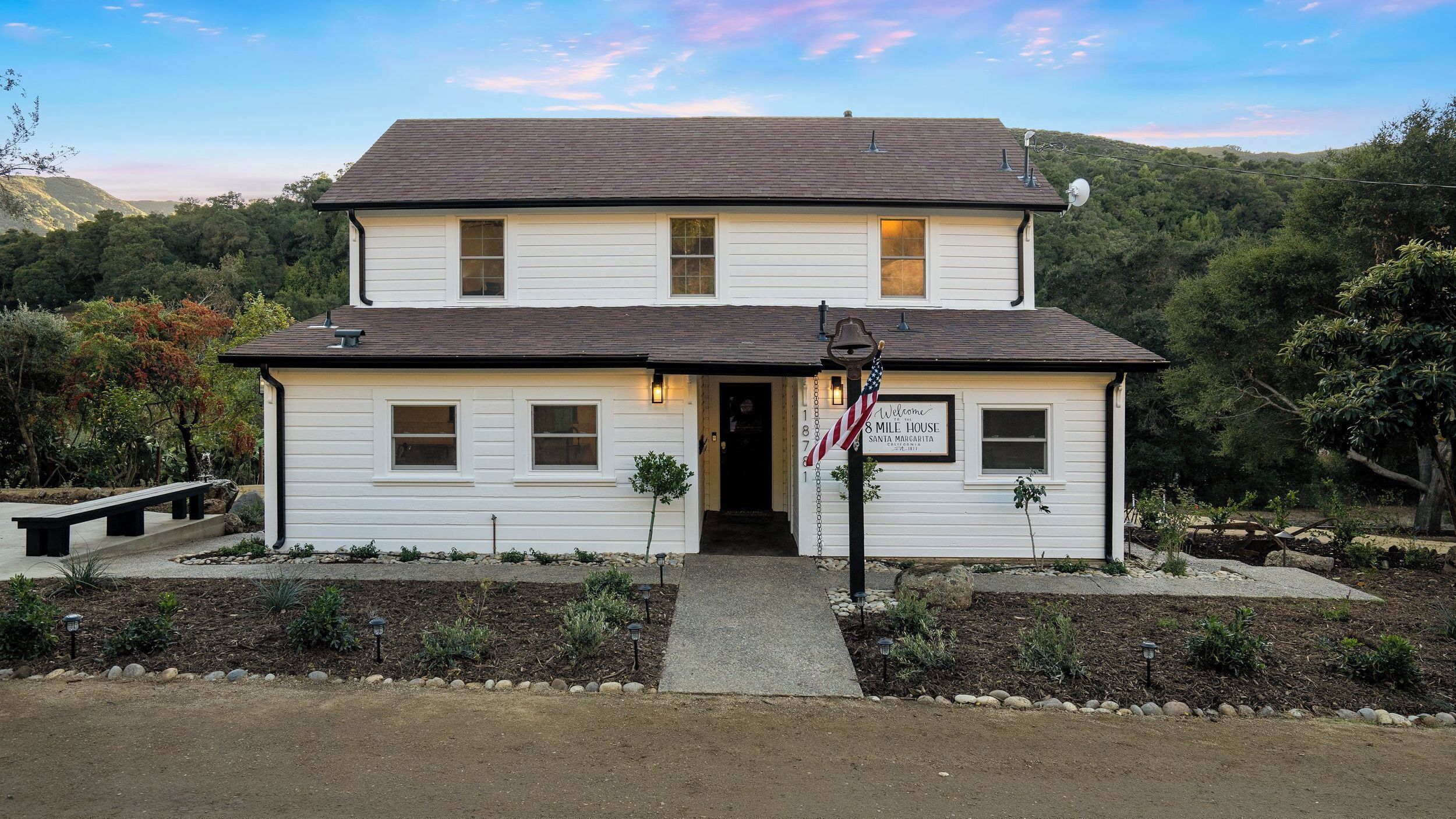 Ein zweistöckiges weißes Haus mit einer Veranda, einem kleinen Garten und einem Schild, das Besucher im 8 Mile House in Santa Margarita, Kalifornien, willkommen heißt.
