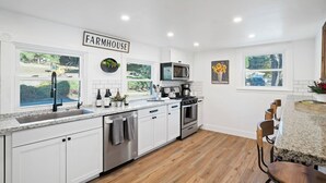 A kitchen with white cabinets, a farmhouse sign, a sink, a stove, and a microwave. - 8 Mile House by Avantstay Historic 1877 Ranch + Party Barn Wine Country (Santa Margarita)