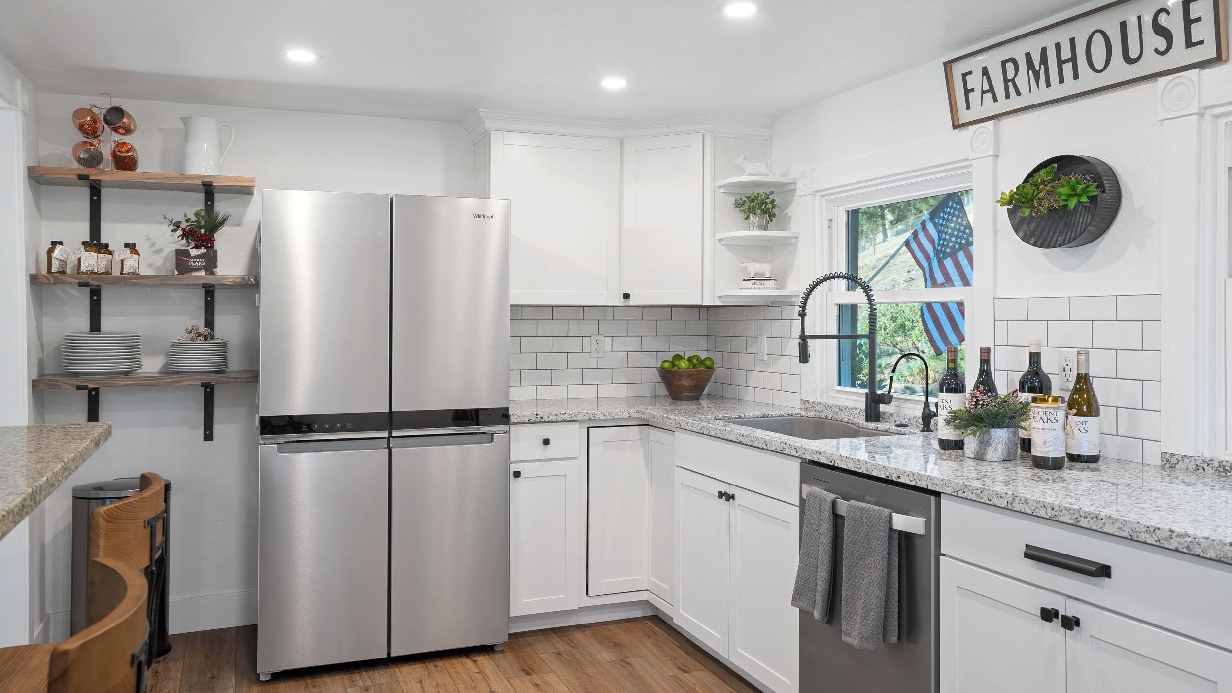 A modern kitchen with white cabinetry, a stainless steel refrigerator, and a farmhouse sign on the wall.