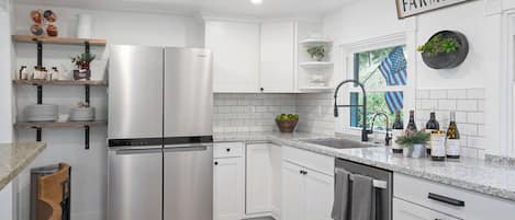 Une cuisine moderne avec des meubles blancs, un réfrigérateur en acier inoxydable et un panneau décoratif de style rustique accroché au mur.