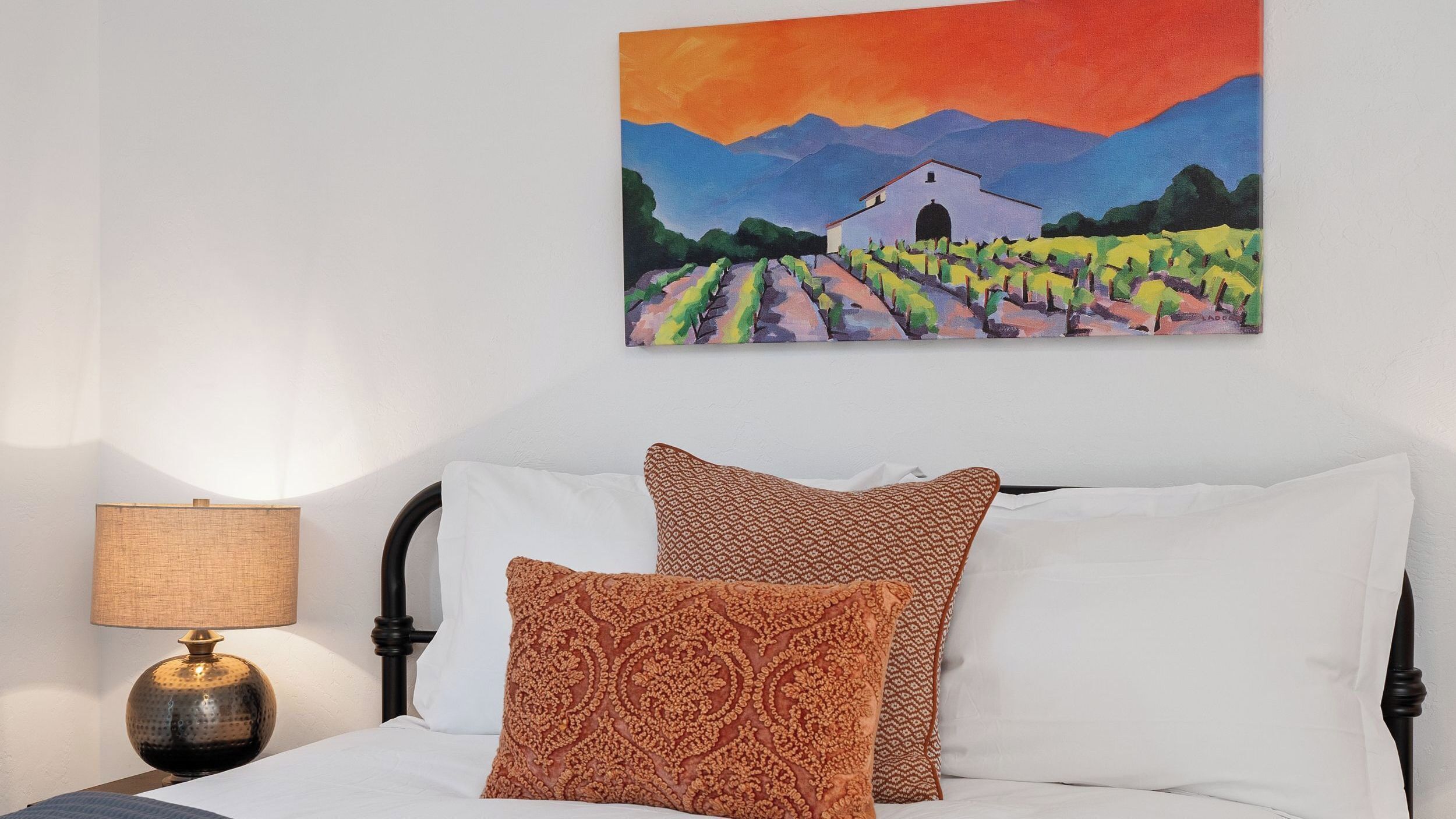 Ein Schlafzimmer mit einem Bett, Kissen, einer Lampe und einem Gemälde an der Wand.