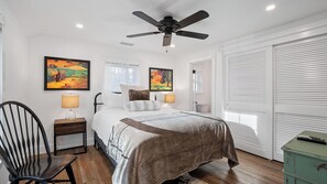 Una camera da letto con un letto, una sedia, una scrivania, una ventola a soffitto e due quadri.