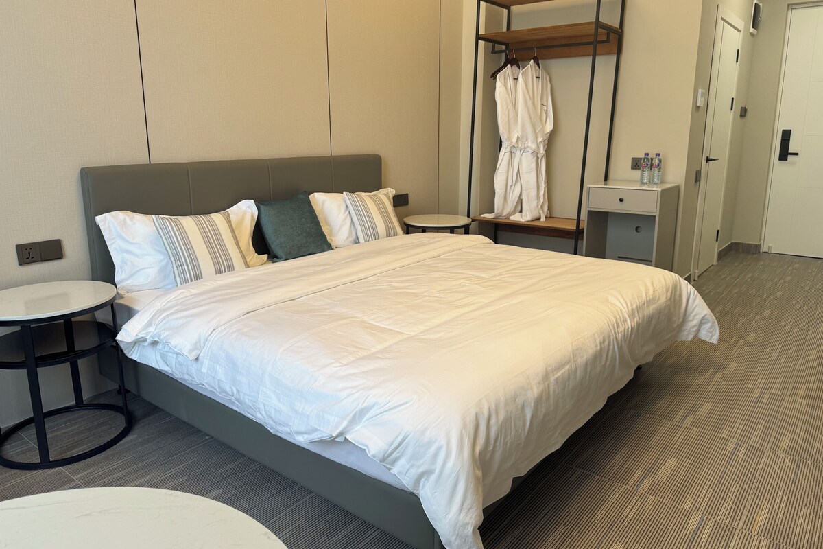 Habitación de hotel con cama, una mesa redonda, un perchero y un escritorio pequeño con una botella.