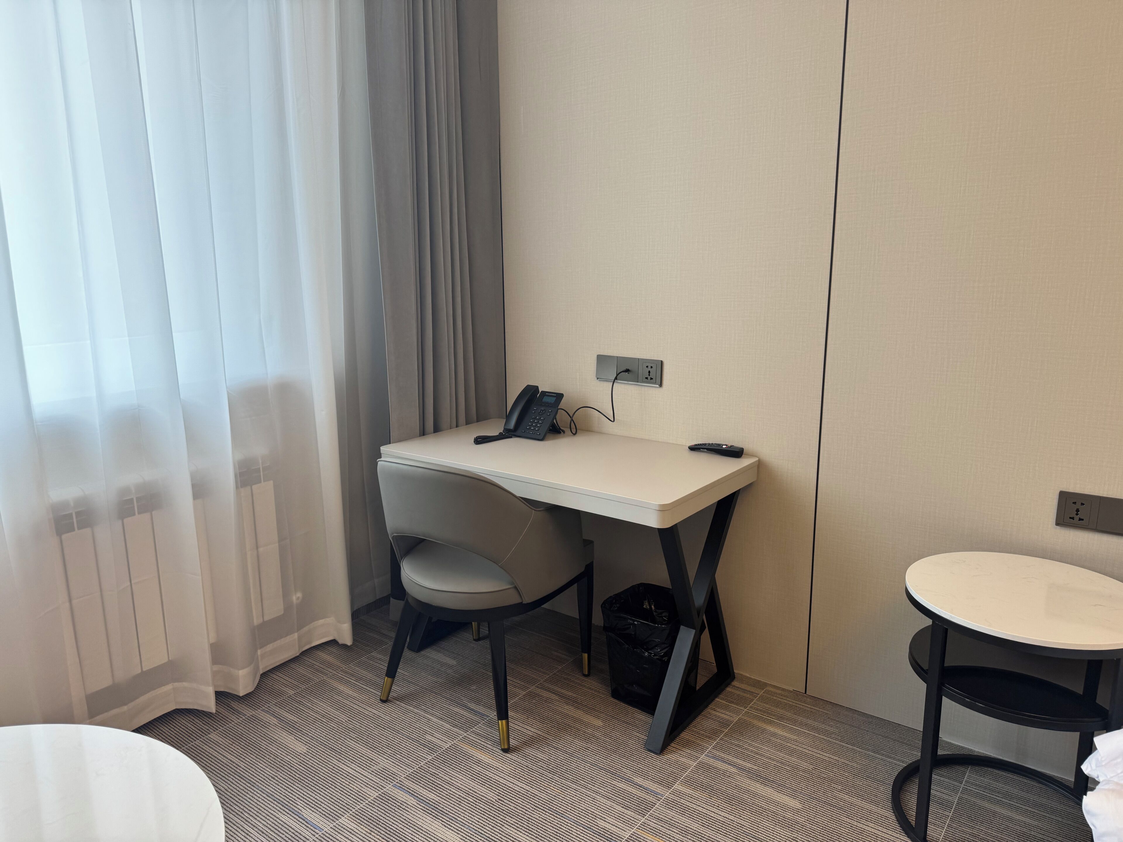 A hotel room with a desk, chair, and a small table.