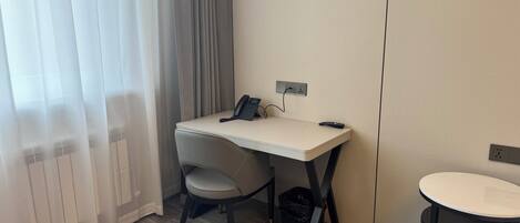 A hotel room with a desk, chair, and a small table.