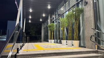 Entrada de edificio con escalones, barandas y plantas en macetas.