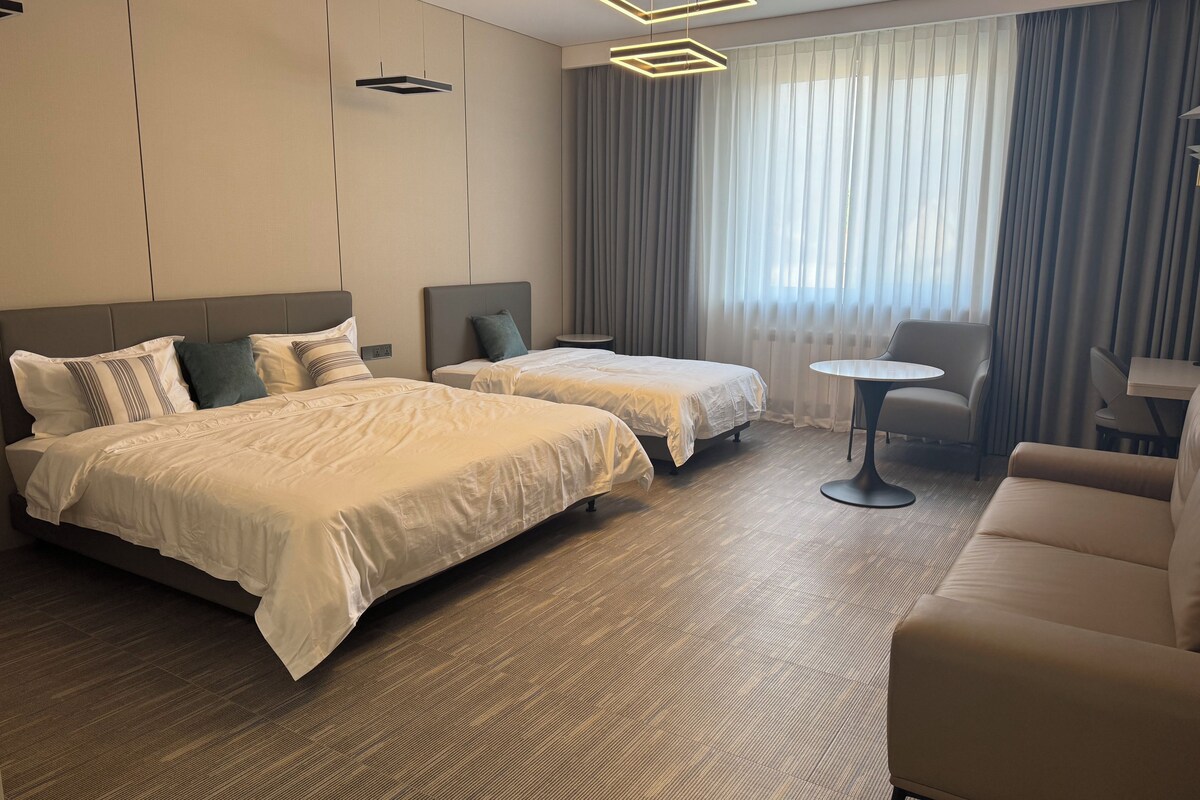 Habitación de hotel con dos camas, una mesa redonda y un sofá.