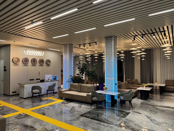 A modern hotel lobby with a reception desk, seating area, and decorative lighting. - Wind Rose hotel (Almaty)