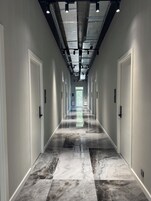 A hallway with a reflective marble floor, white doors, and a ceiling with exposed ductwork and lighting fixtures.