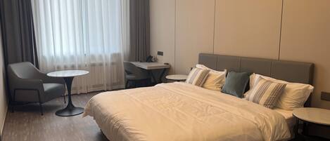 A hotel room with a large bed, a desk, a chair, and a small table.