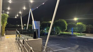 An outdoor area with a covered walkway, a parking lot, and a street with streetlights. - Wind Rose hotel (Almaty)