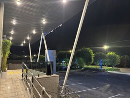 Un espacio exterior con un corredor cubierto, estacionamiento y una calle con farolas.