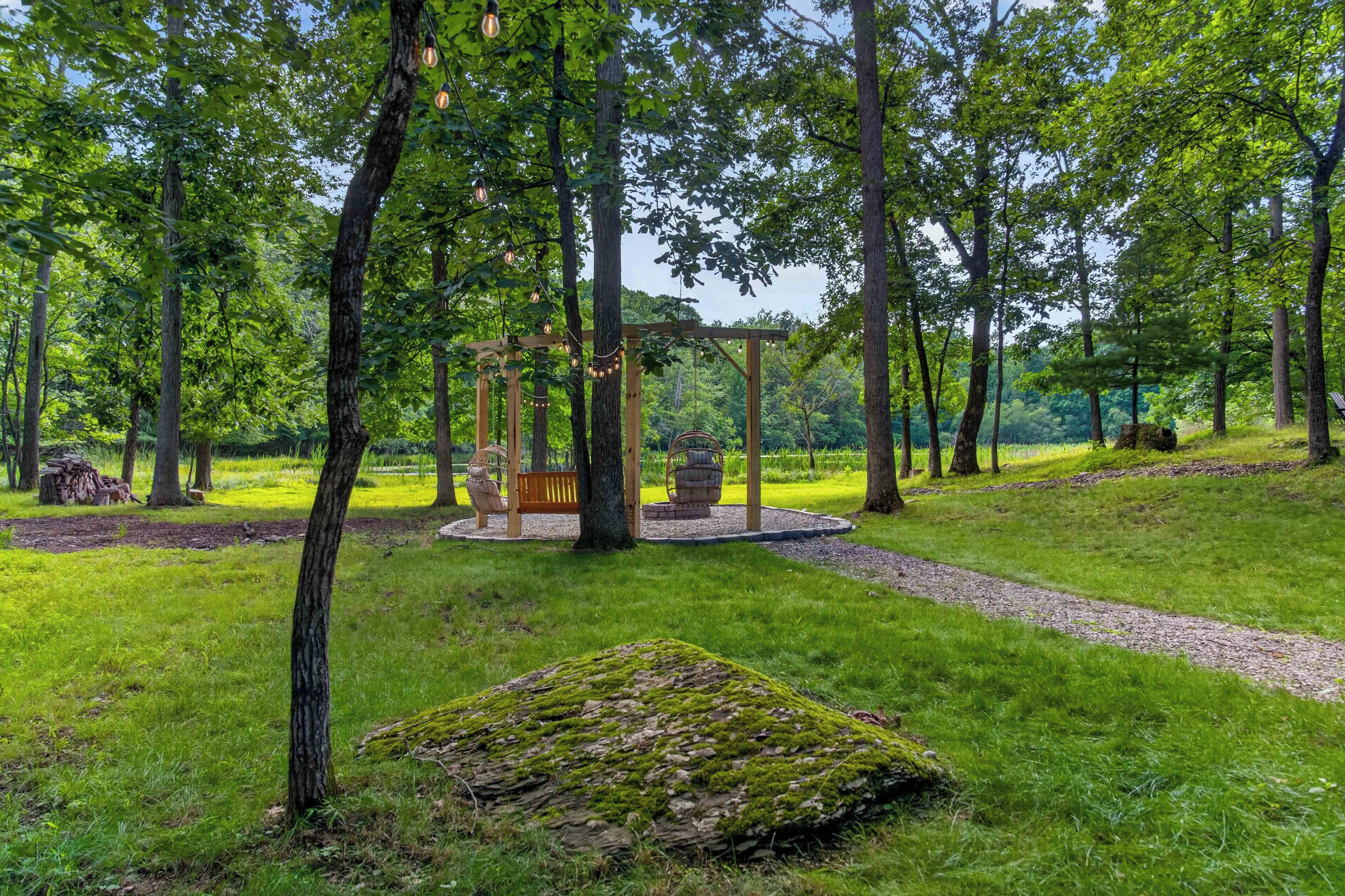 Ein friedlicher Park mit einer hölzernen Schaukel, einer Feuerstelle aus Stein und einem moosbewachsenen Baumstamm.