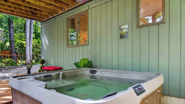 Ein Whirlpool in einem überdachten Außenbereich mit Holzterrasse, einem roten Kissen und einem Fenster mit Sicherheitshinweis.