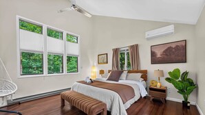Ein Schlafzimmer mit Bett, Nachttischen, einem Hängekorbstuhl, einer Bank, einer Topfpflanze und einem Deckenventilator.