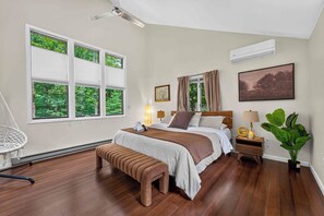 Une chambre à coucher comprenant un lit, des tables de chevet, un fauteuil suspendu, un banc, une plante en pot et un ventilateur de plafond.